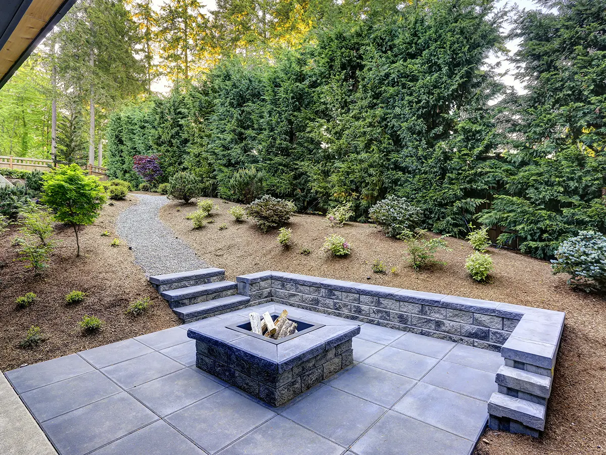 Large paver patio in backyard with mulch and tall trees