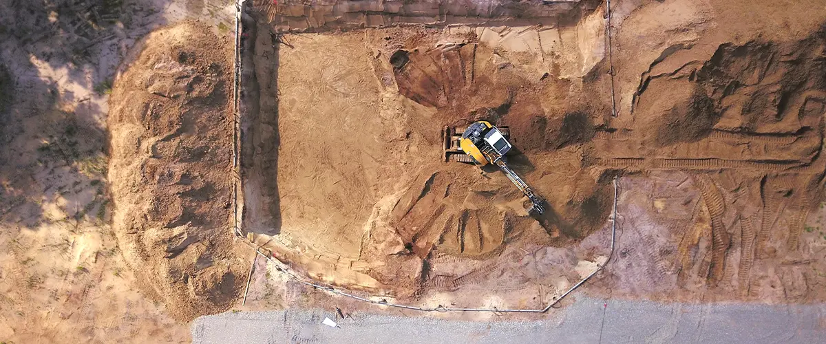 Aerial view of an excavator preparing the foundation for a building project, highlighting detailed site preparation work.