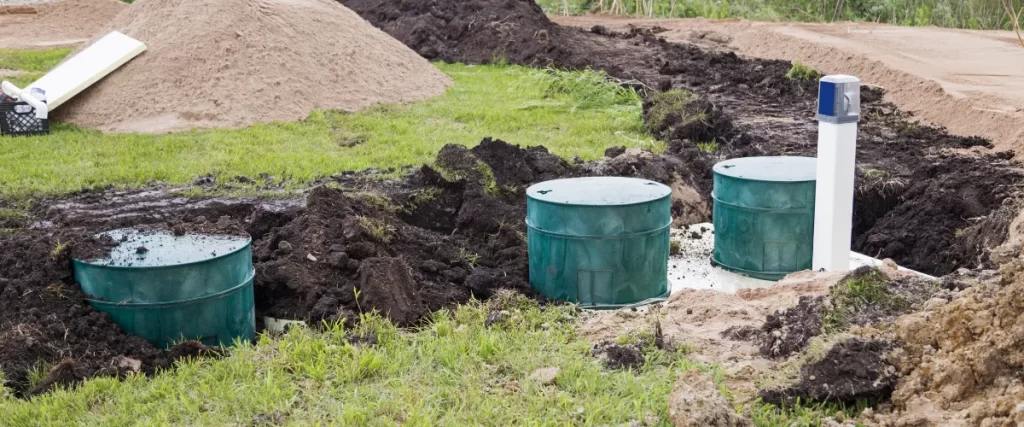 Partially installed green septic tank in a grassy area with surrounding dirt piles.