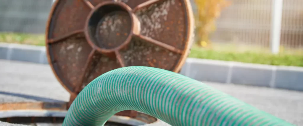 Close-up of a septic tank lid with a large hose inserted for pumping.