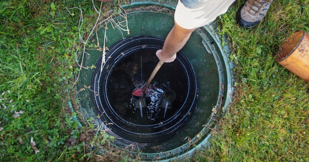 Person reaching into an open septic tank for maintenance or inspection.