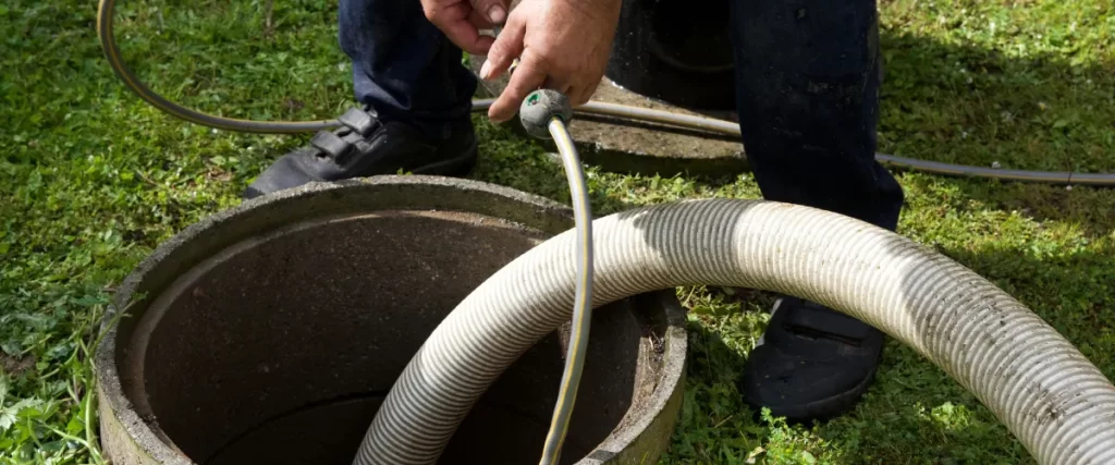 Worker using a vacuum hose to clean or empty a septic tank, wearing gloves for safety.