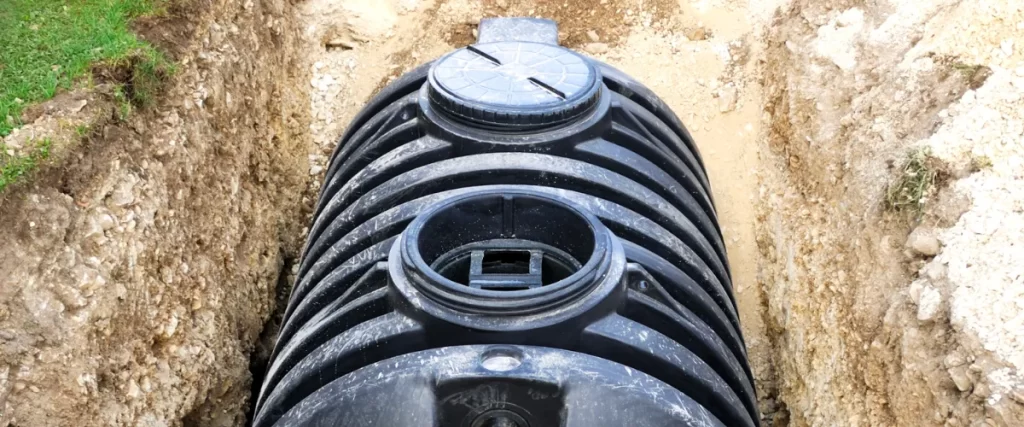 Close-up of a black plastic septic tank with multiple access lids, partially buried in the ground.