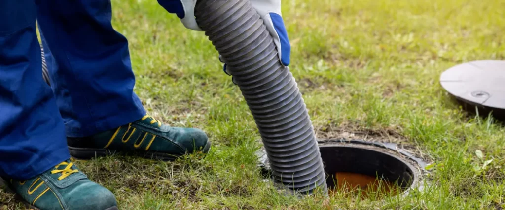 Person in blue gloves holding a large hose to pump waste from an underground septic tank.