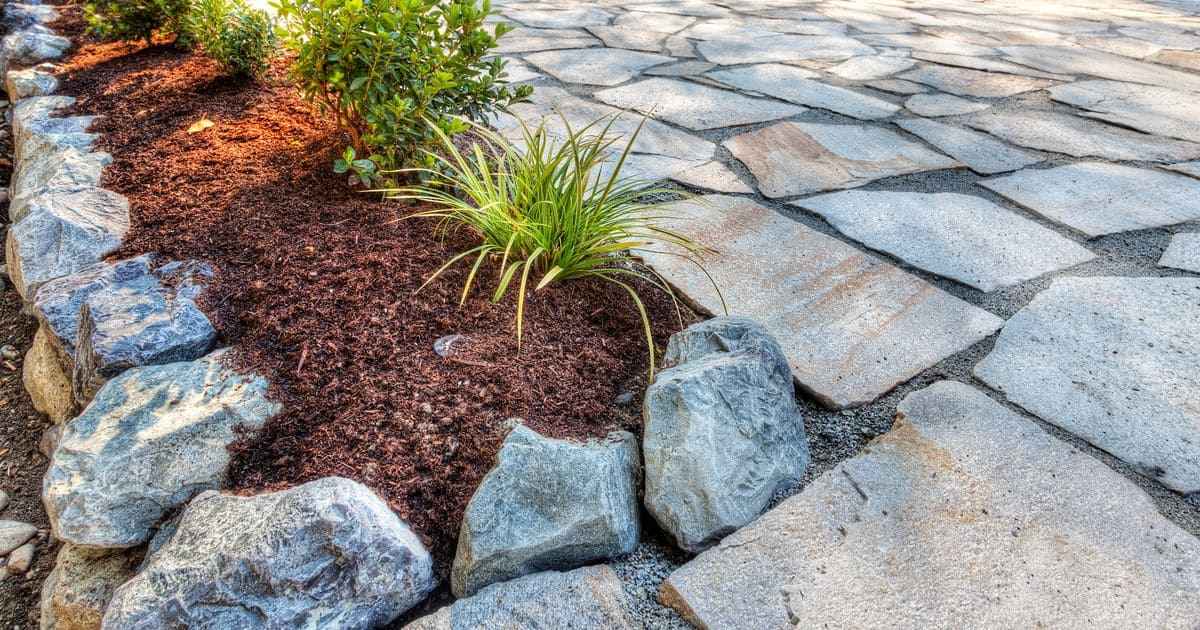 Water-wise landscaping featuring an irregular flagstone patio, large decorative rock border, and drought-tolerant ornamental grasses set in mulch.