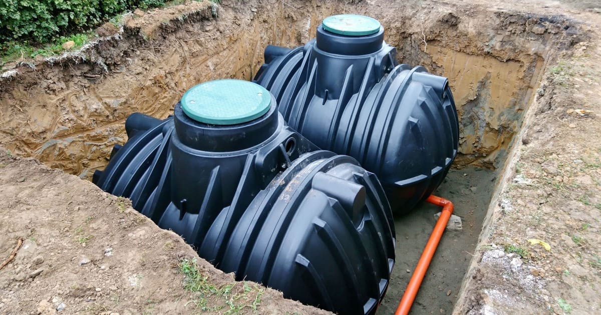 Professional underground installation of two black plastic dual-chamber septic tanks in a prepared excavation pit, meeting local septic tank installation requirements.