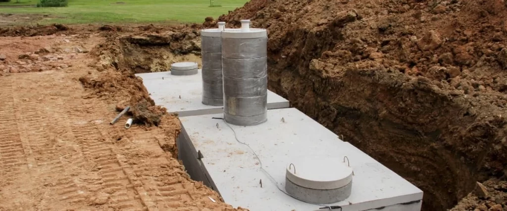 Heavy-duty concrete septic tanks installed in a wide trench with tall grey risers extending toward the surface level before final grading.