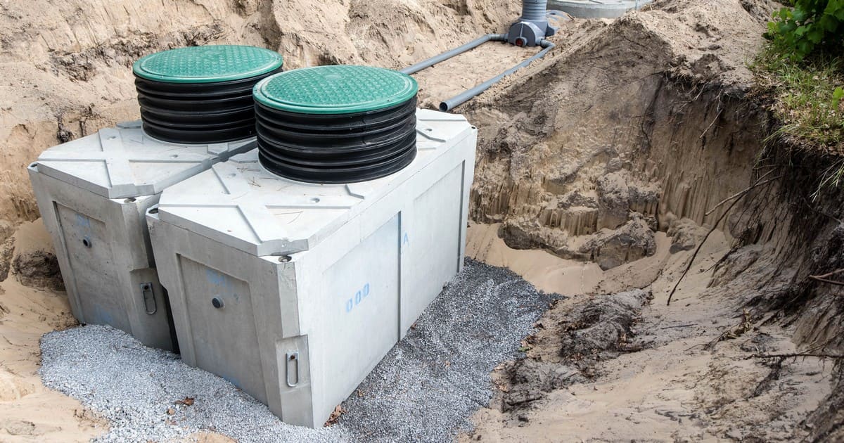 Professional septic system installation featuring two large concrete septic tanks placed in a prepared excavation site with green riser lids.