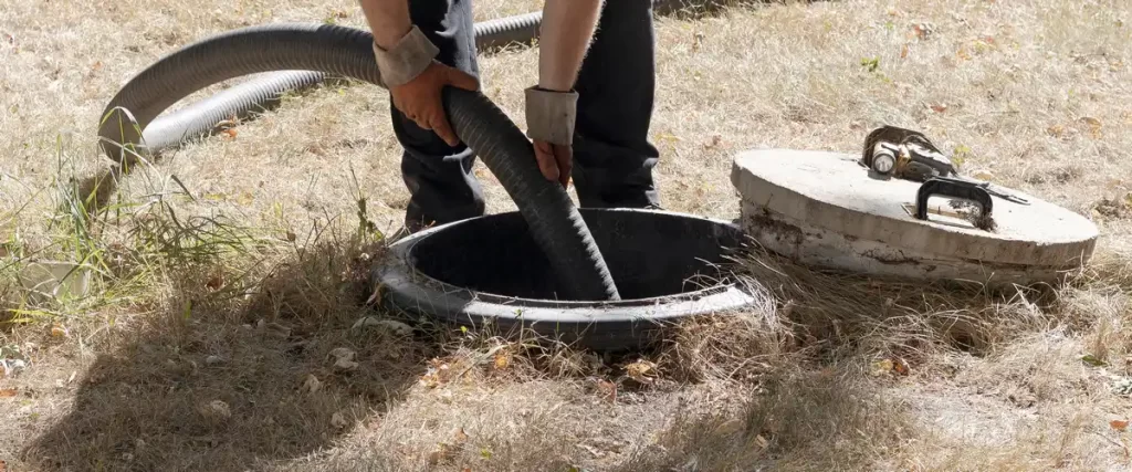 A service technician inserting a heavy-duty vacuum hose into an open septic tank for professional pumping and waste removal.