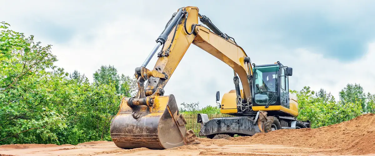 A large yellow excavator with a heavy-duty bucket moving earth and dirt during a site excavation project.
